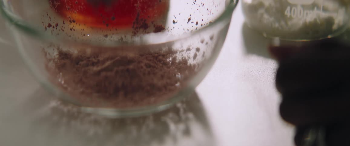 Person adds powder to small glass bowl sitting on reflective white surface