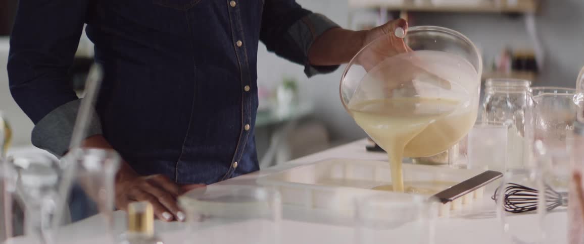 A person in a shop pours liquid soap into a mold in order to shape it into bars
