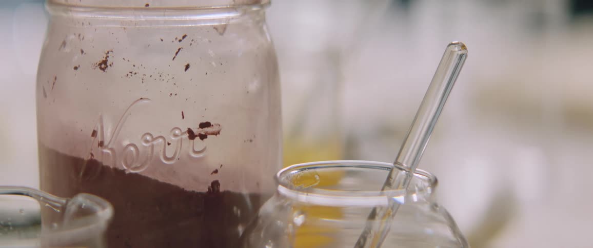 Glass utensil sits in a jar next to a larger jar containing a brown substance