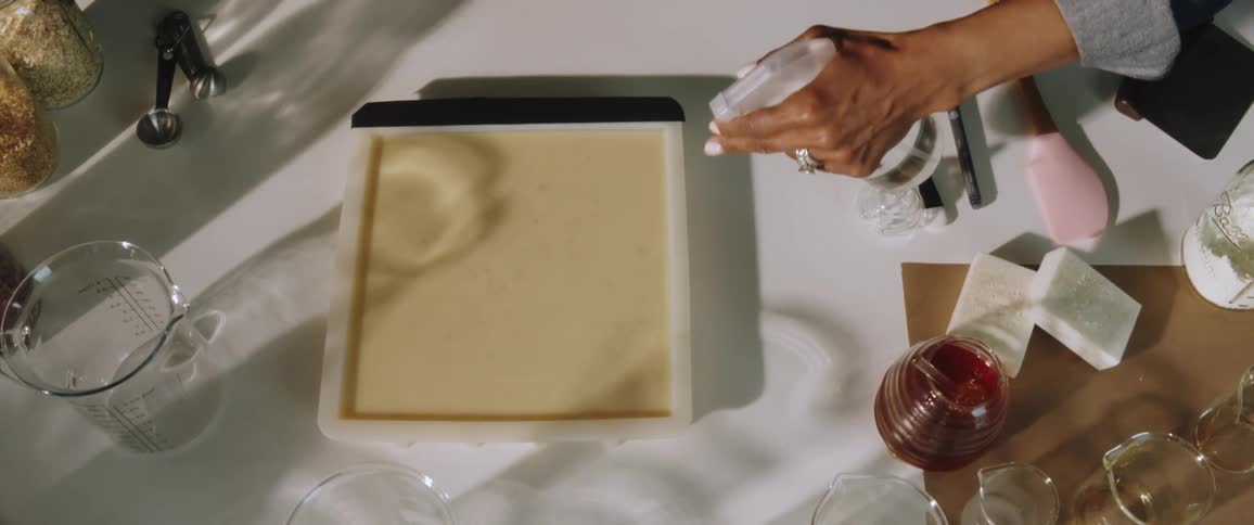 A woman holds a spray bottle and uses it to moisten the top of soap in a mold