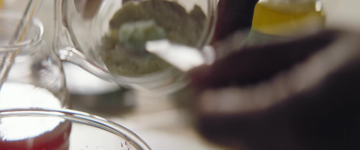A person adding ingredients to a glass bowl with a measuring spoon