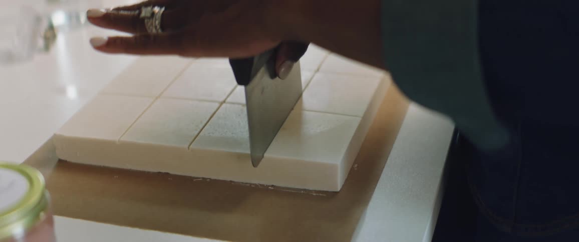 A woman uses a large blade to cut bars of soap