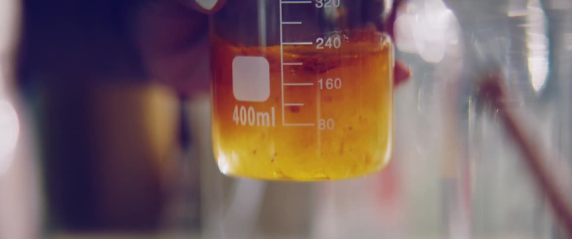 A woman uses a glass stirrer to mix oils in a beaker