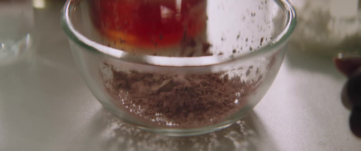 Cocoa powder is dropped into a glass mixing bowl
