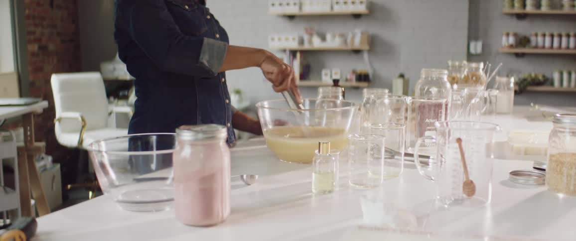 A woman in a room mixing a batter in a bowl with a whisk with a wall and window in the background