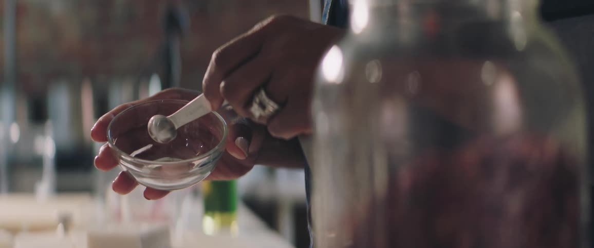 Woman uses metal measuring spoon to add ingredient to small glass bowl
