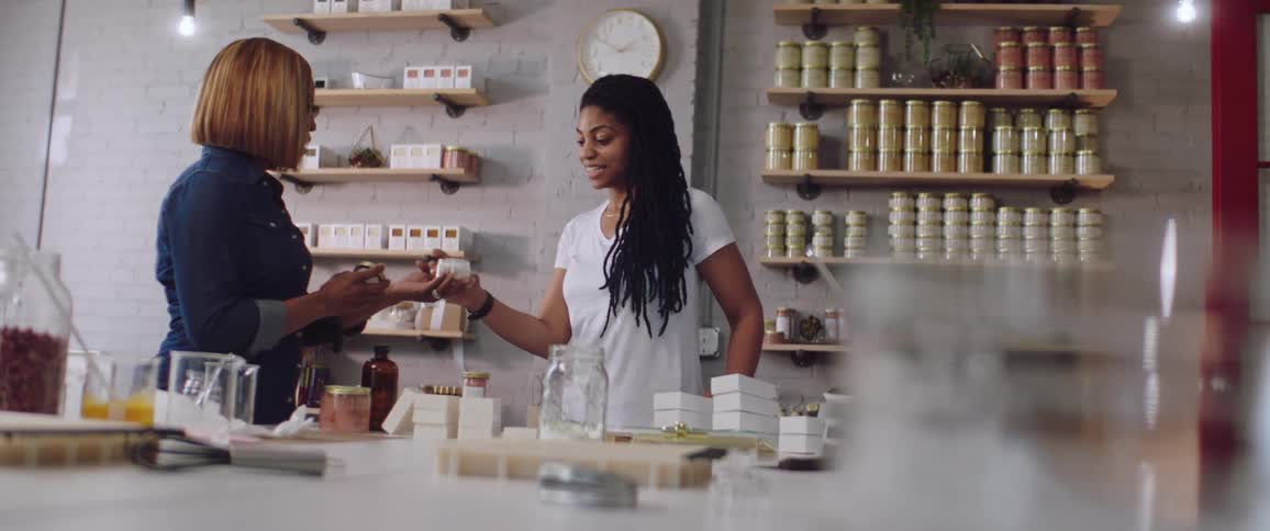 A woman hands a customer a candle to smell in an apothecary store