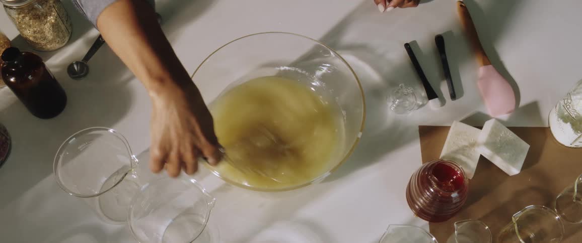 A hand blends ingredients in a glass bowl with a whisk