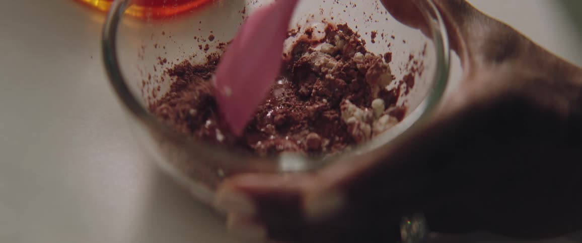 A woman holds a small glass bowl and mixes ingredients with a pink spatula