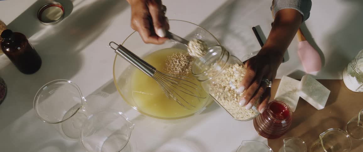 A woman uses a measuring spoon to scope oatmeal from a jar into a mixing bowl