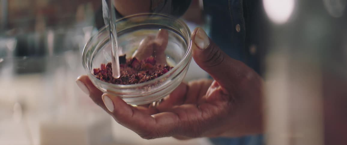 A woman holds a glass mortar and pestle and stirs crushed leaves and herbs