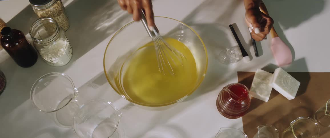 A woman making soap whisks oils in a glass bowl