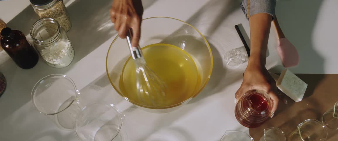 Woman adds honey to mixture in glass mixing bowl before stirring mixture with metal whisk
