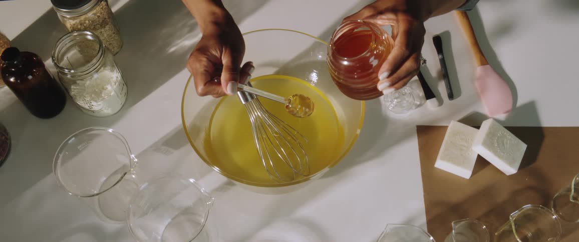 The woman in a room adding honey into a bowl with a whisk and liquid