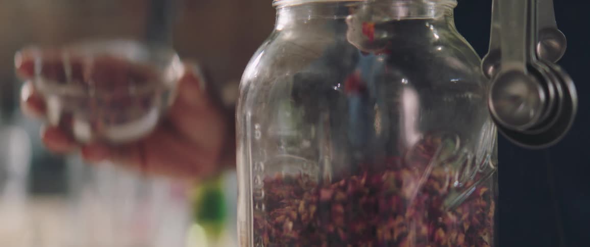 A person scooping ingredients from a glass jar with measuring spoons