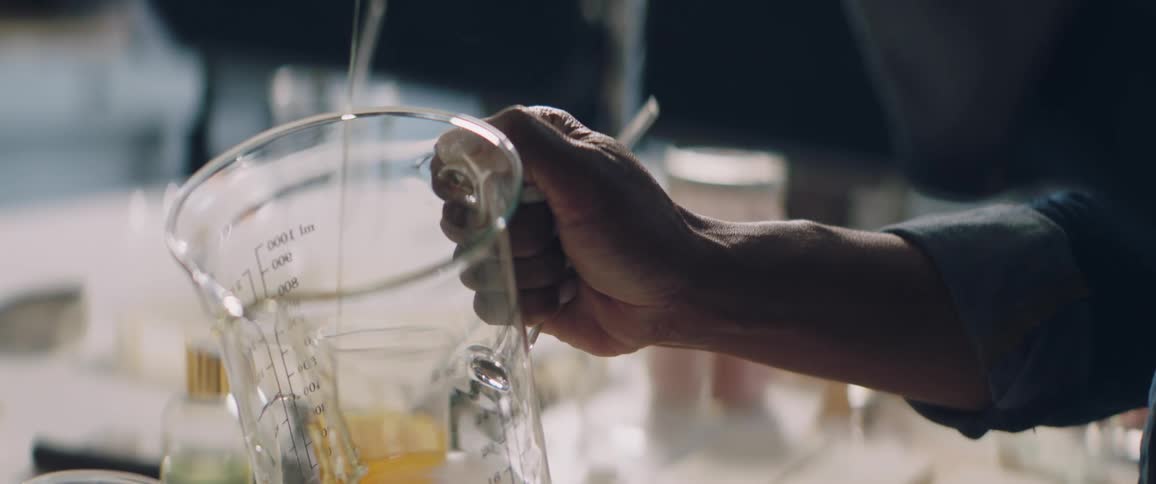 A woman adds honey from a jar to a glass beaker