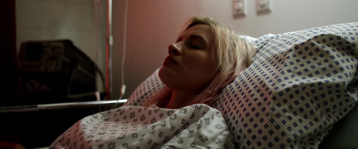 Blonde woman lays in a hospital bed as an intravenous stand sits next to her