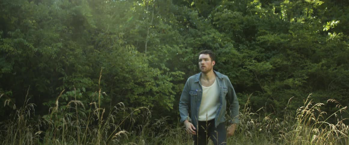 Bearded man walks out of a forest and across a field