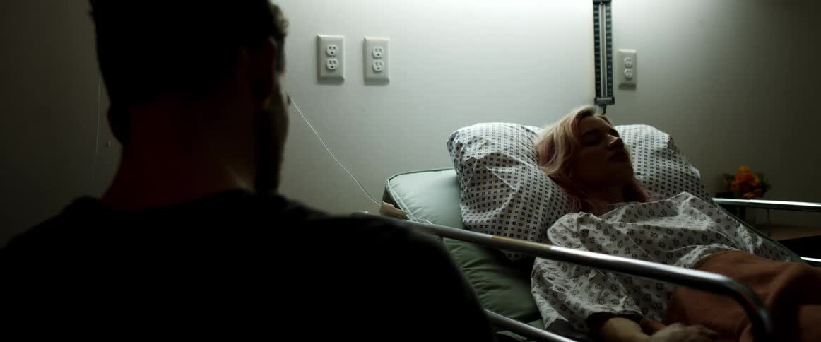 Man sits next to woman lying asleep in hospital bed with iv tubing trailing to her