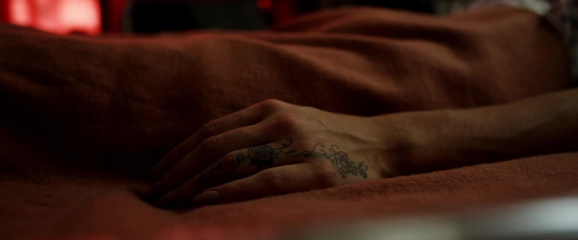 A person is laying still and only their hand is visible with a small tattoo on it