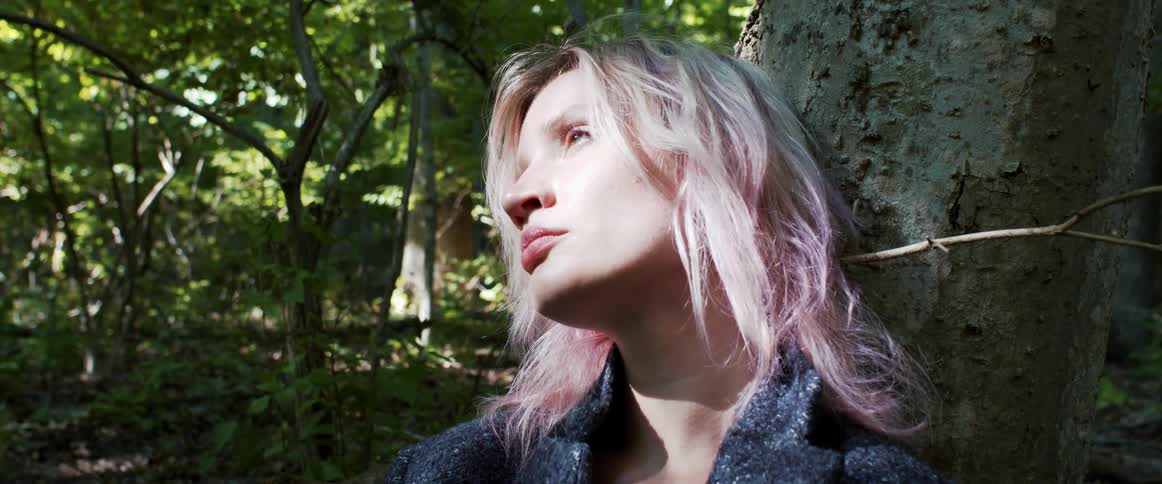 Sunlight shines on a womans forest as she leans against a tree in the forest