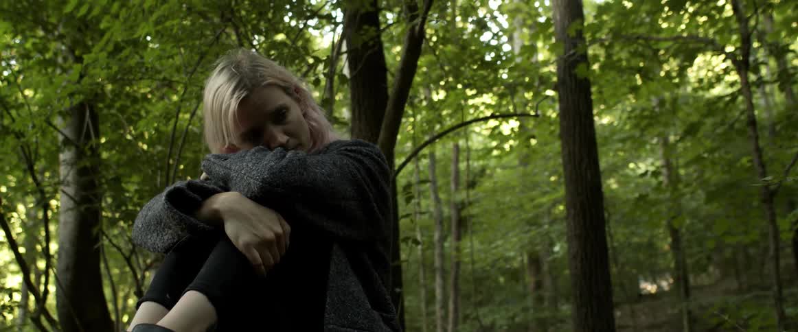 A woman rests her head on her arms as she sits in a forest