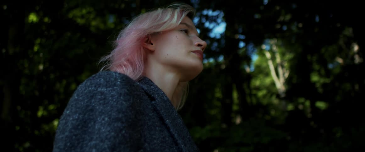 A young woman leisurely walks beneath trees outdoors during the day