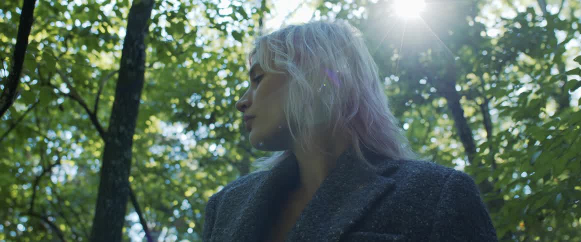 A woman standing in a forest with trees the sky and clouds in the background