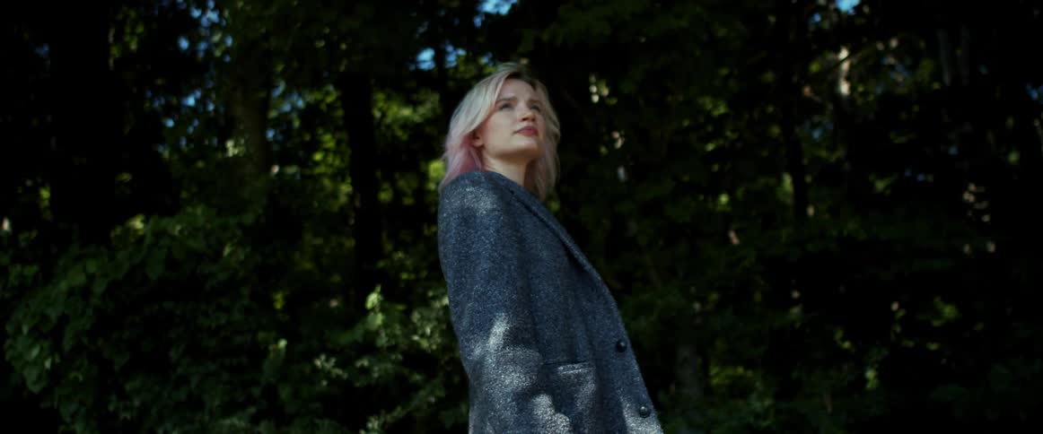 A woman stands and walks in front of a line of trees in a forest