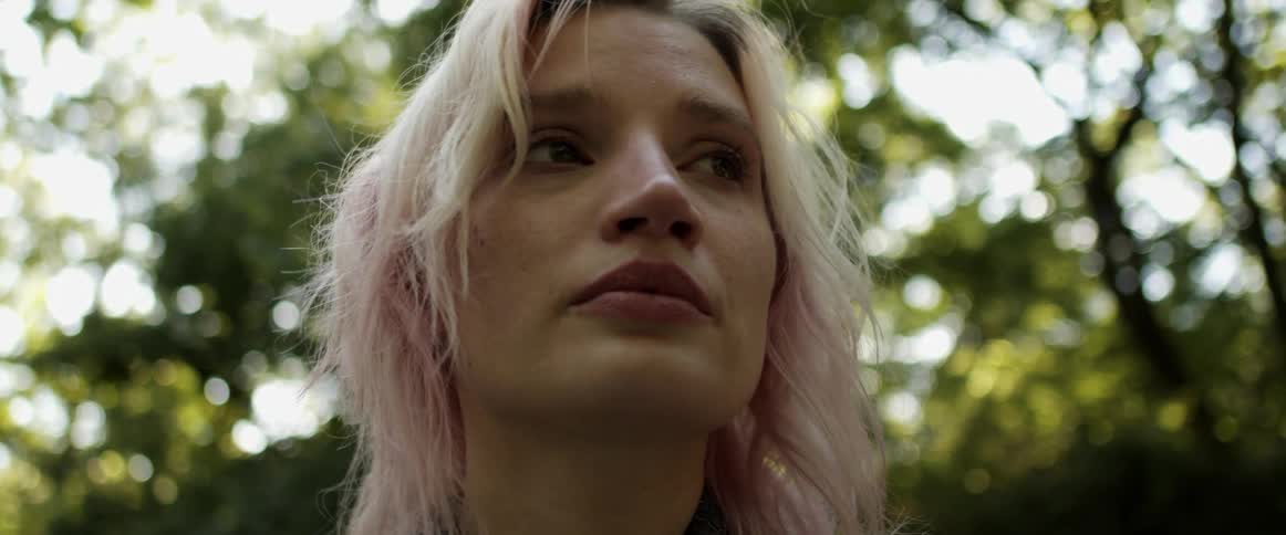 A woman is standing outdoors in a wooded area