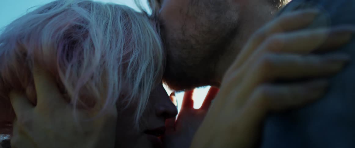 A man kissing a woman on her forehead with the sky and clouds in the background