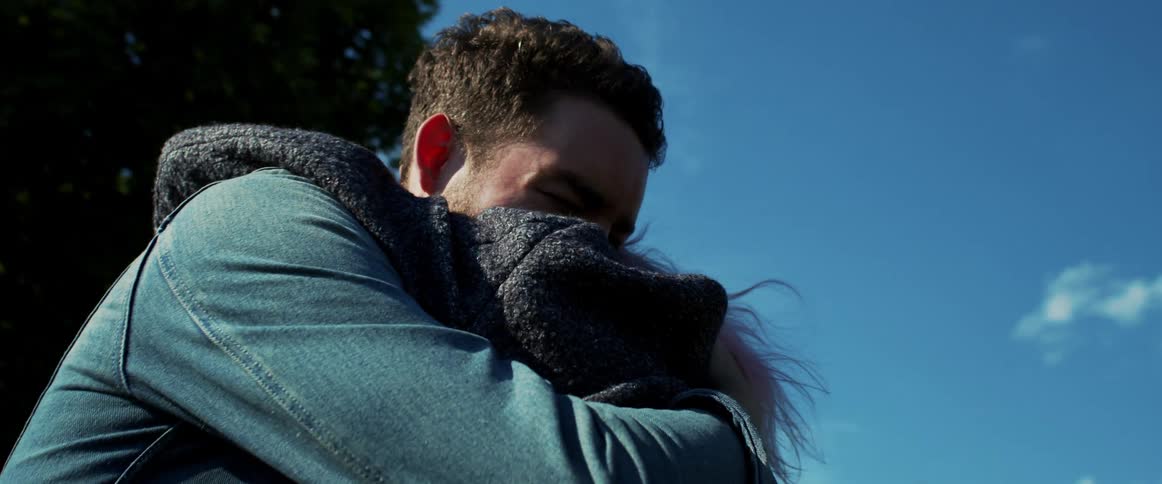 A young couple hold each other in a tight hug while standing outdoors near trees