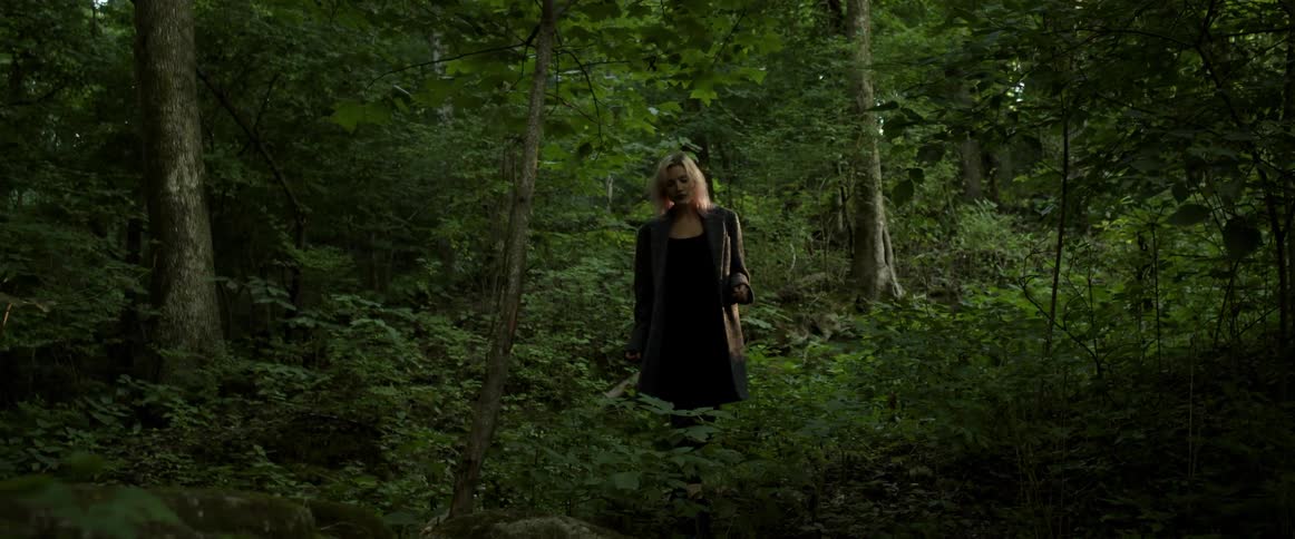 A woman carefully walks through a forest while glancing around at her surroundings during the day