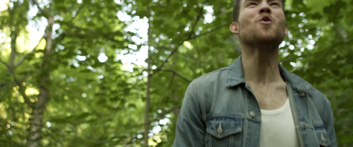 A man in a denim jacket screaming outside near trees