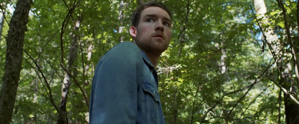 A young man walking in the forest turns around and looks behind him