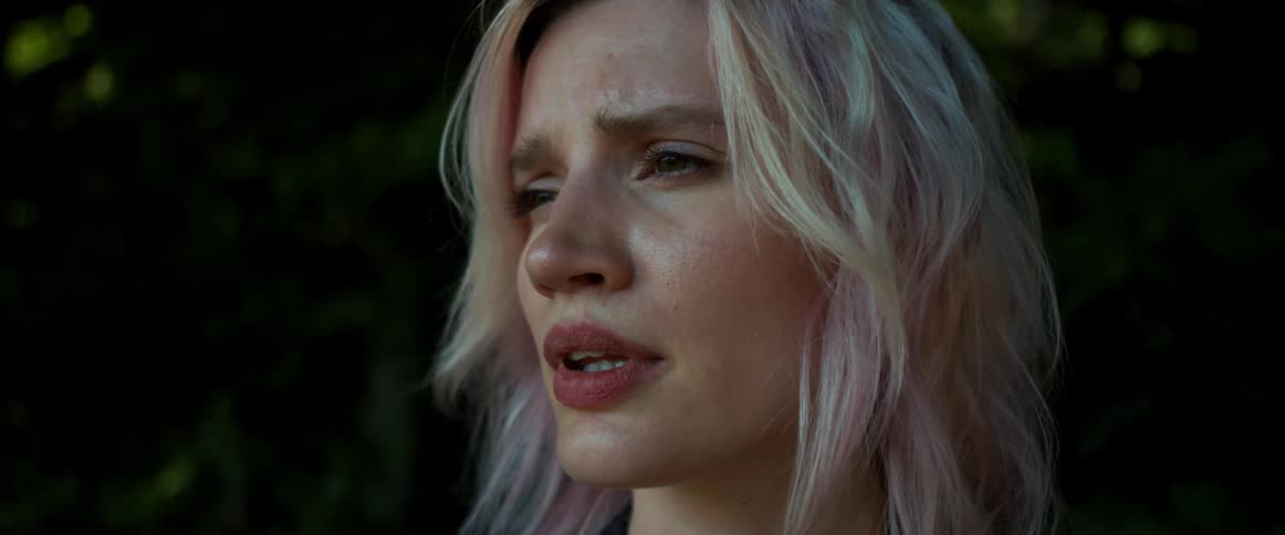 A woman with dyed hair looks around at the trees in an anxious fashion