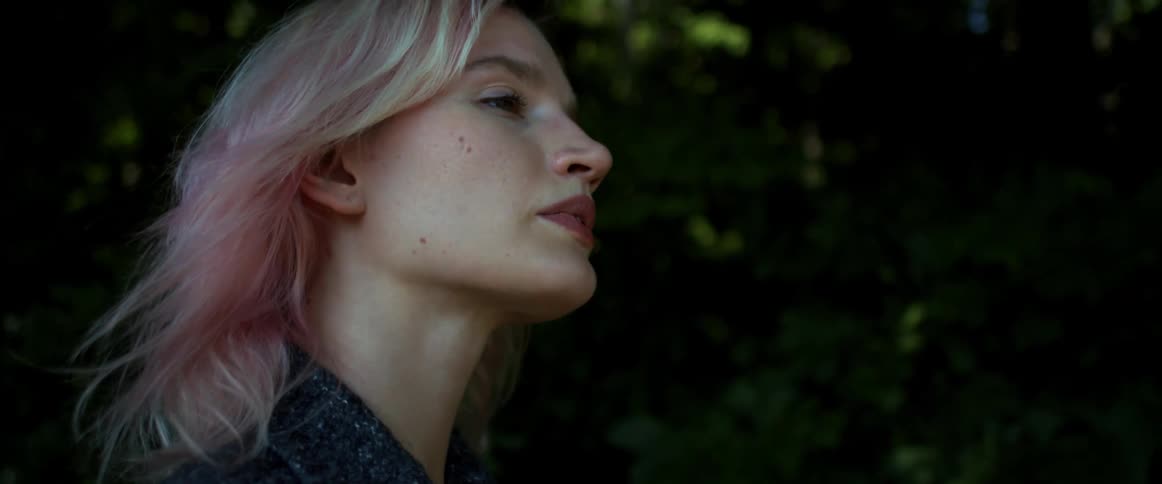 Blonde woman with pink tinted hair walks past trees