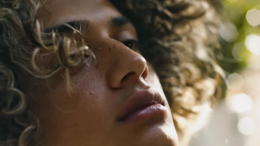 A young man with long and curly hair swipes it out of his face