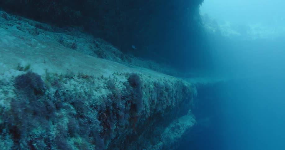 Light shines through circular hole in wreck based coral reef as fish swim