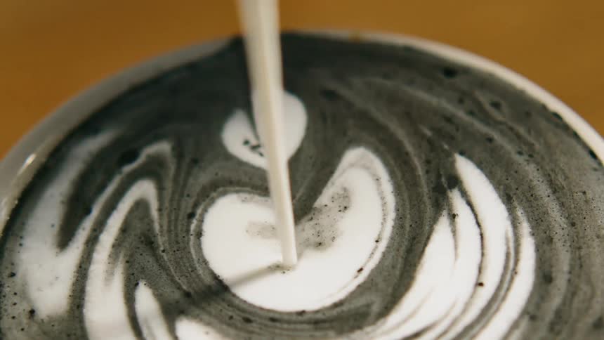 Cream being poured into a cup of coffee on a table