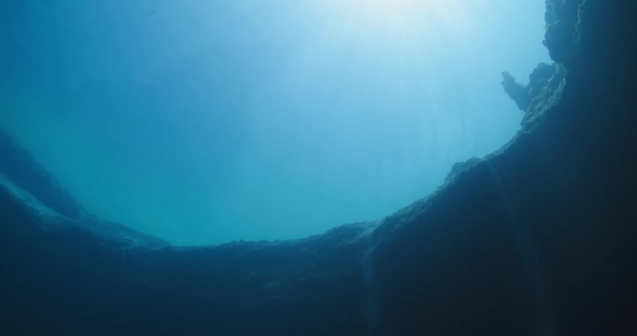 Underwater in the ocean would rocks with the sky and sun above
