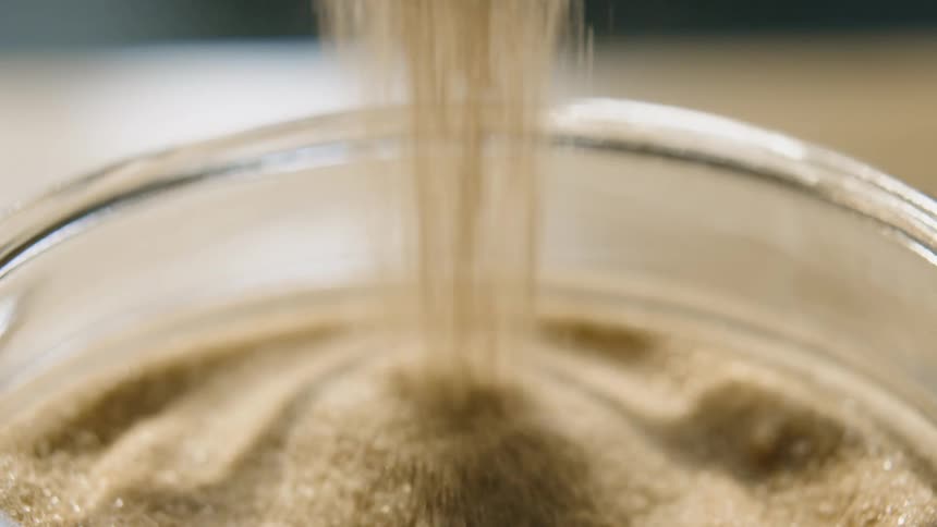 Sugar is being poured into a glass bowl