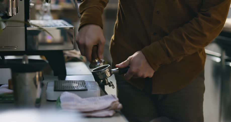 A man uses a tool to prepare coffee behind a counter in a cafe during the day