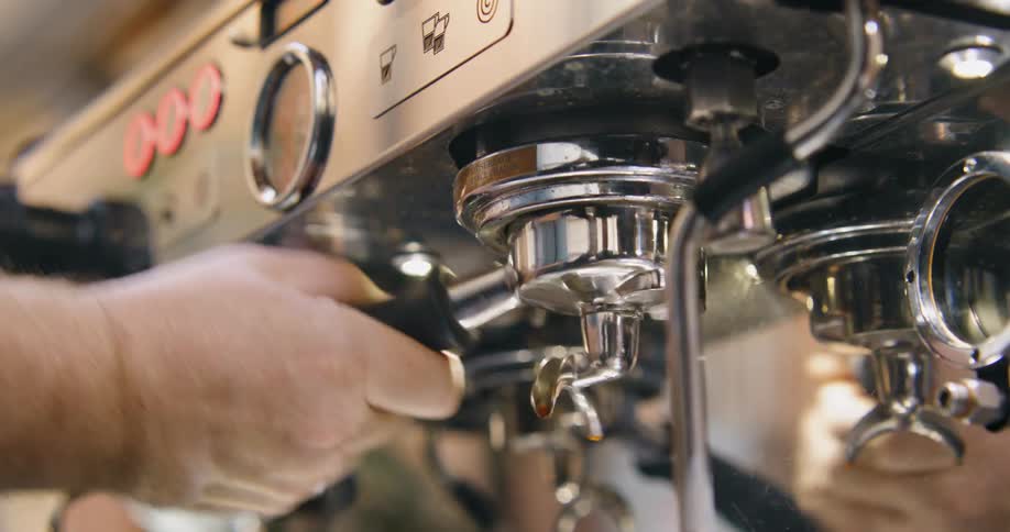 A man removes the portafilter on an espresso machine as he cleans