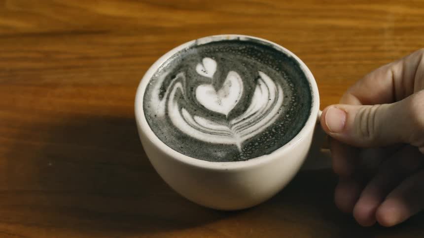 A person in a room placing a cup of coffee and cream on a table