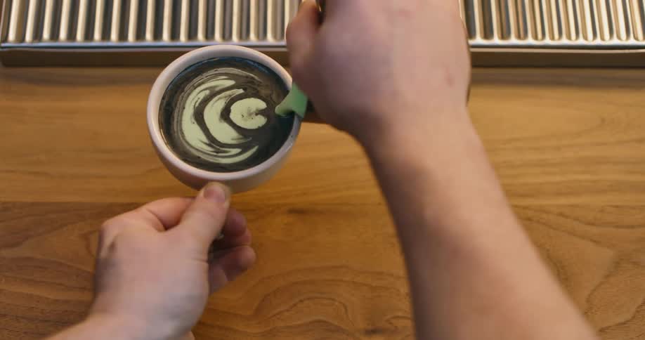 A man uses frothed milk to create a design in a cup of matcha