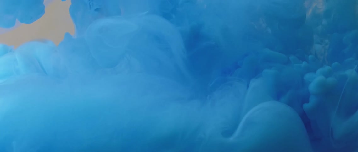 Waves and blobs of bright blue ink floating on a tank of clear water