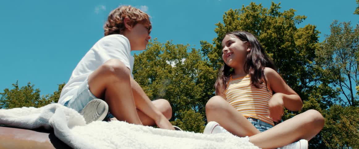 A boy and girl play red hands while sitting together on a blanket outdoors on a sunny day