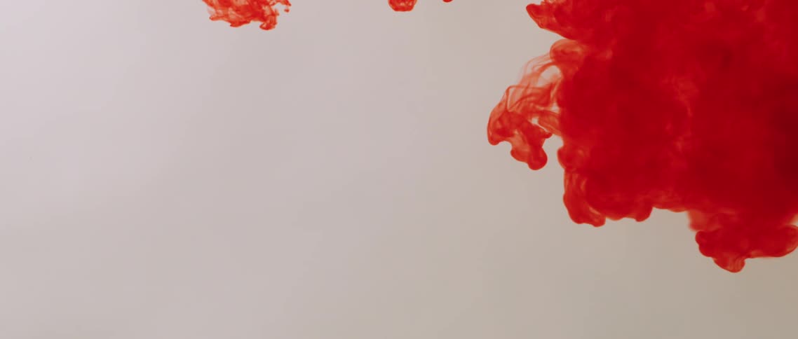 A red powder slowly explodes and spreads against a white wall