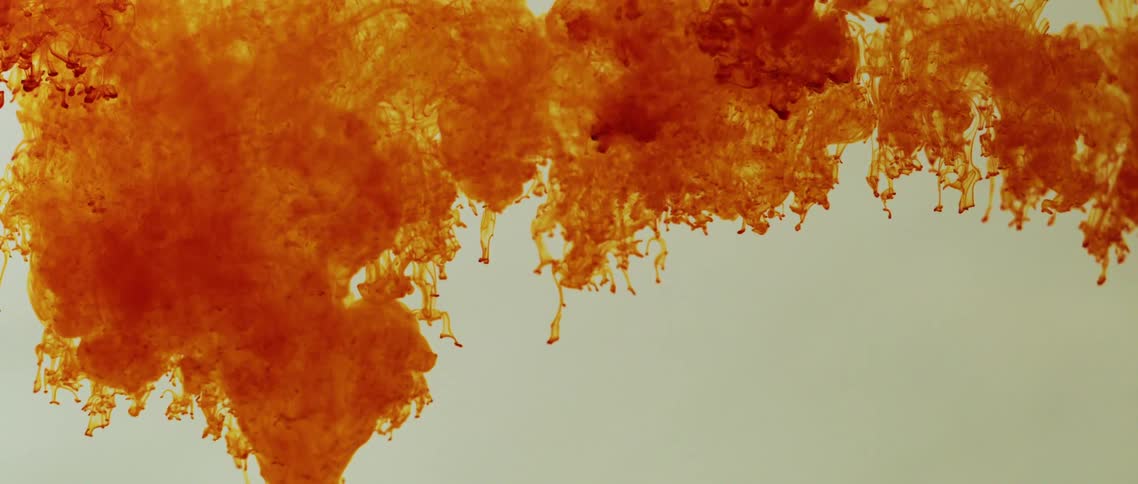 Red and orange bright ink flowing down inside a tank of clear water